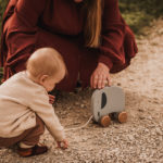 Kleinkind beim Familienfotoshooting spielt mit einem hölzernen Elefanten zum ziehen.