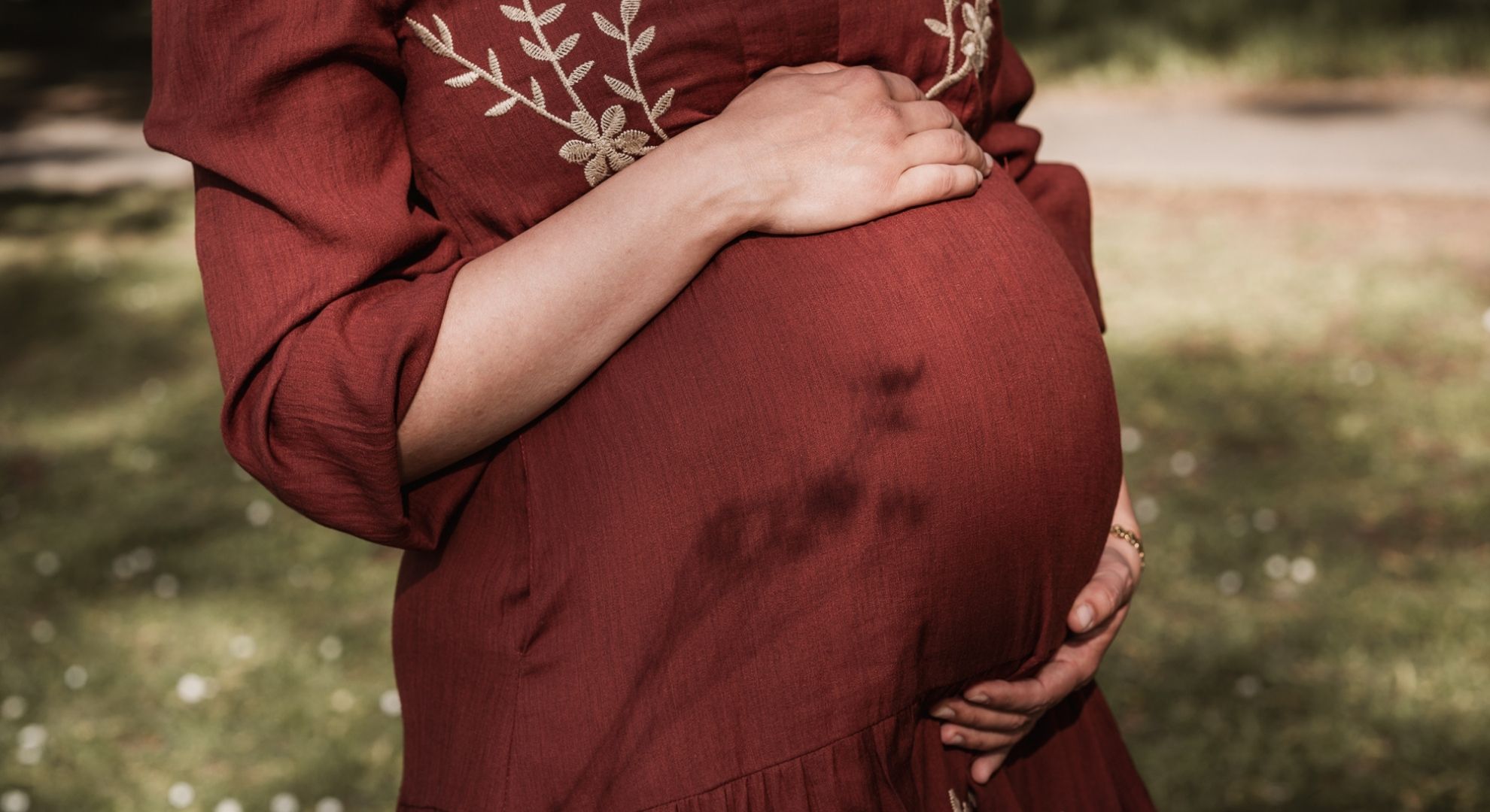 Nahaufnahme eines Babybauchs mit Schattenspiel auf rostrotem Kleid
