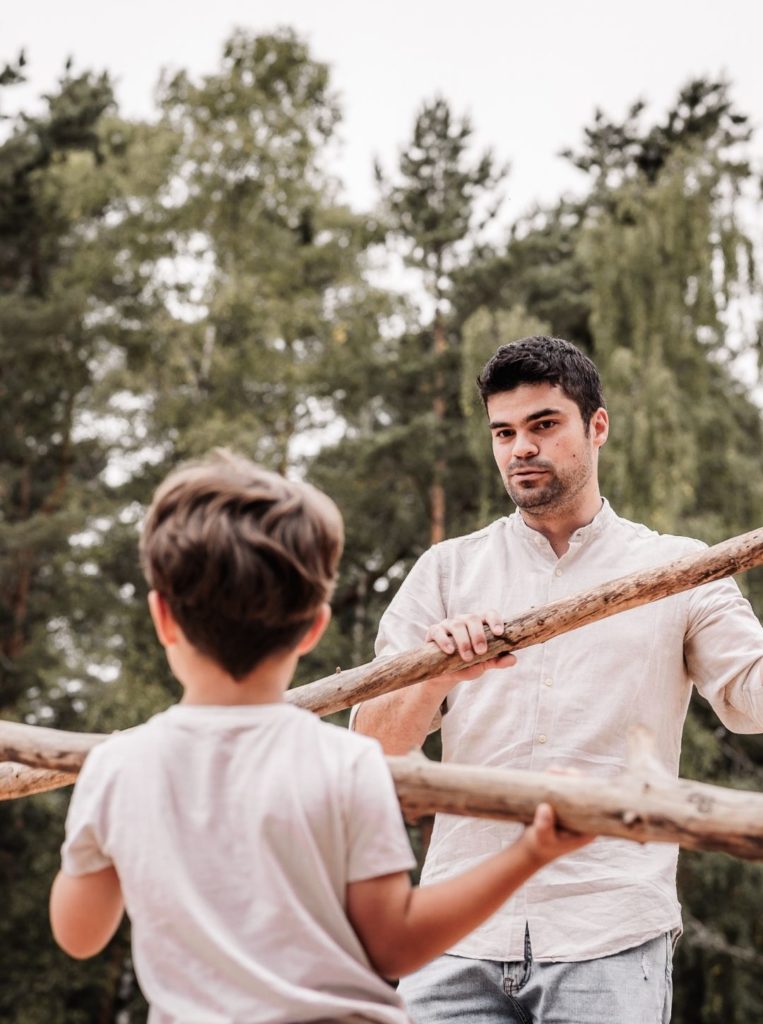 Papa und Sohn im Wald mit "Speeren" aus Baumstämmen. Sie haben ein Abenteuer bei einem Familienfotoshooting-Ausflug.