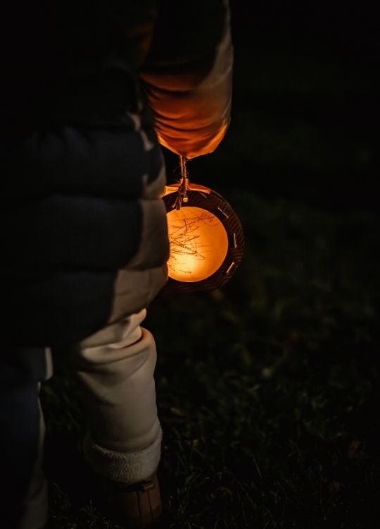 Laterne in der Dunkelheit. Ein kleines Kind hält diese in den Händen.