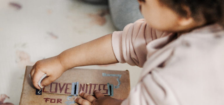 Kleines Alltags-Ritual für Familien: Ein kleines Mädchen steckt eine Liebesnotiz in eine selbstgebastelte Box für ihre Familie.