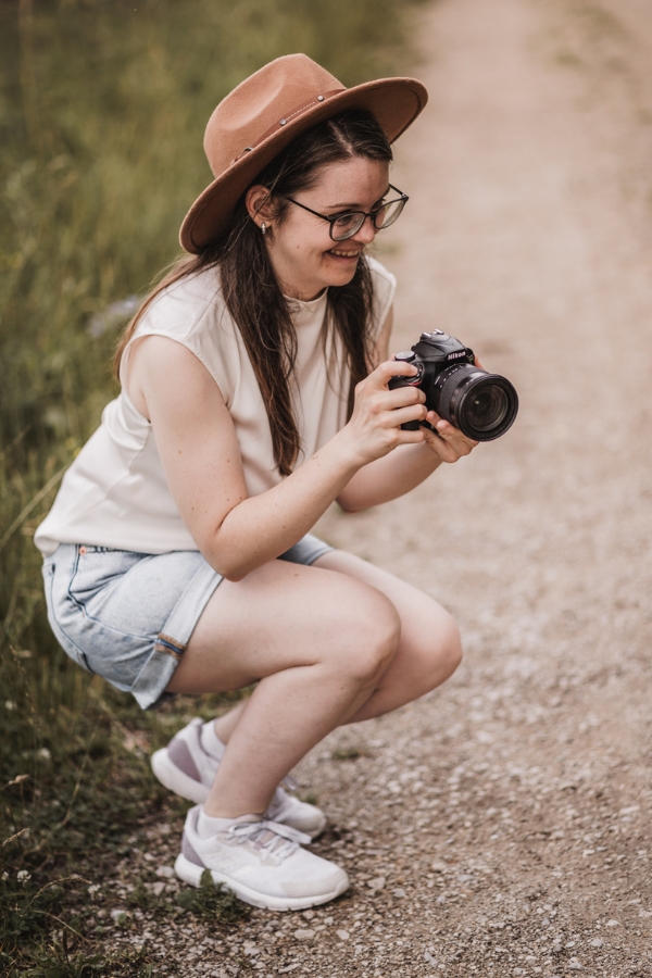 Stefie - Familienfotografin in Nürnberg, Fürth und Umgebung. Auf dem Foto ist die Fotografin bei ihrer Arbeit zu sehen. Sie hält trägt einen Hut und hält ihre Kamera in den Händen.