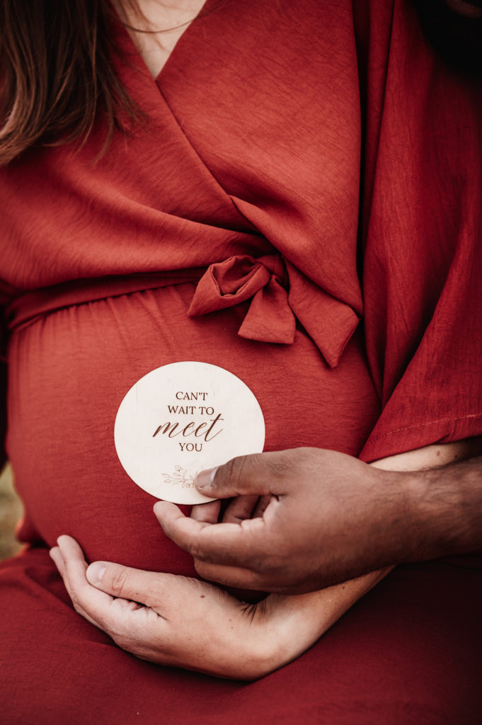 Nahaufnahme von Babybauch mit Kärtchen "Can't wait to meet you"