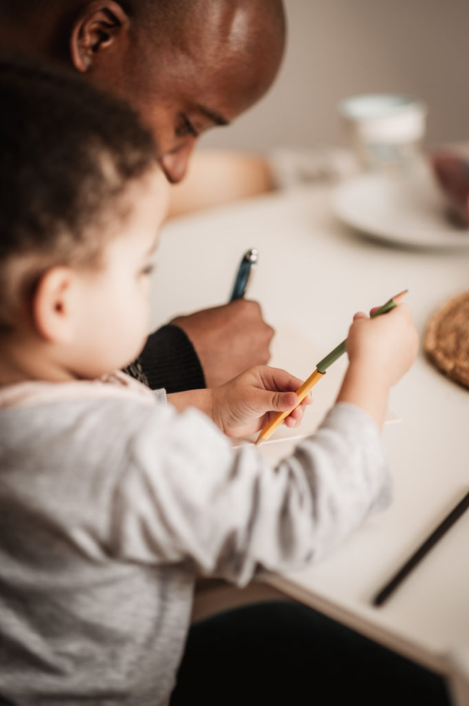 Papa und Tochter am Esstisch machen zusammen eine Karte.