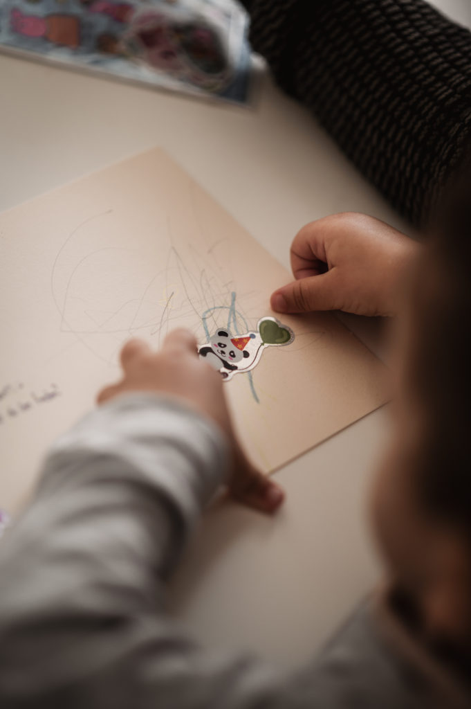 Das Foto zeigt die Hände eines kleinen Kindes, das einen Sticker auf eine Karte klebt.