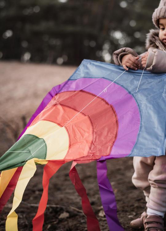 Knallbunter Drachen in Kinderhänden draußen in der Natur.