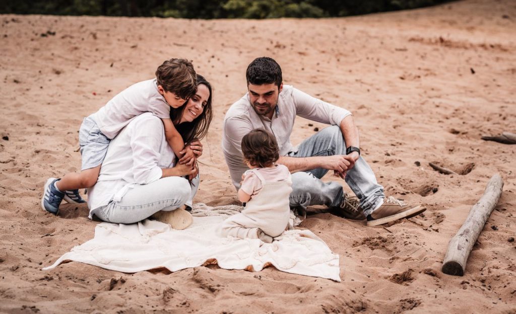 Familie mit 2 Kindern, junge und mädchen, auf einer Sanddüne in Nürnberg beim Familienfotoshooting. Sie lachen und kuscheln miteinander.