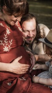 Familie mit werdender Mama und kleinem Kind auf einer Picknickdecke im Park