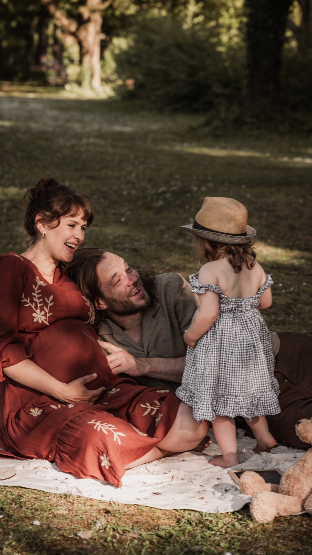 Familie mit werdender Mama und kleinem Kind auf einer Picknickdecke im Park