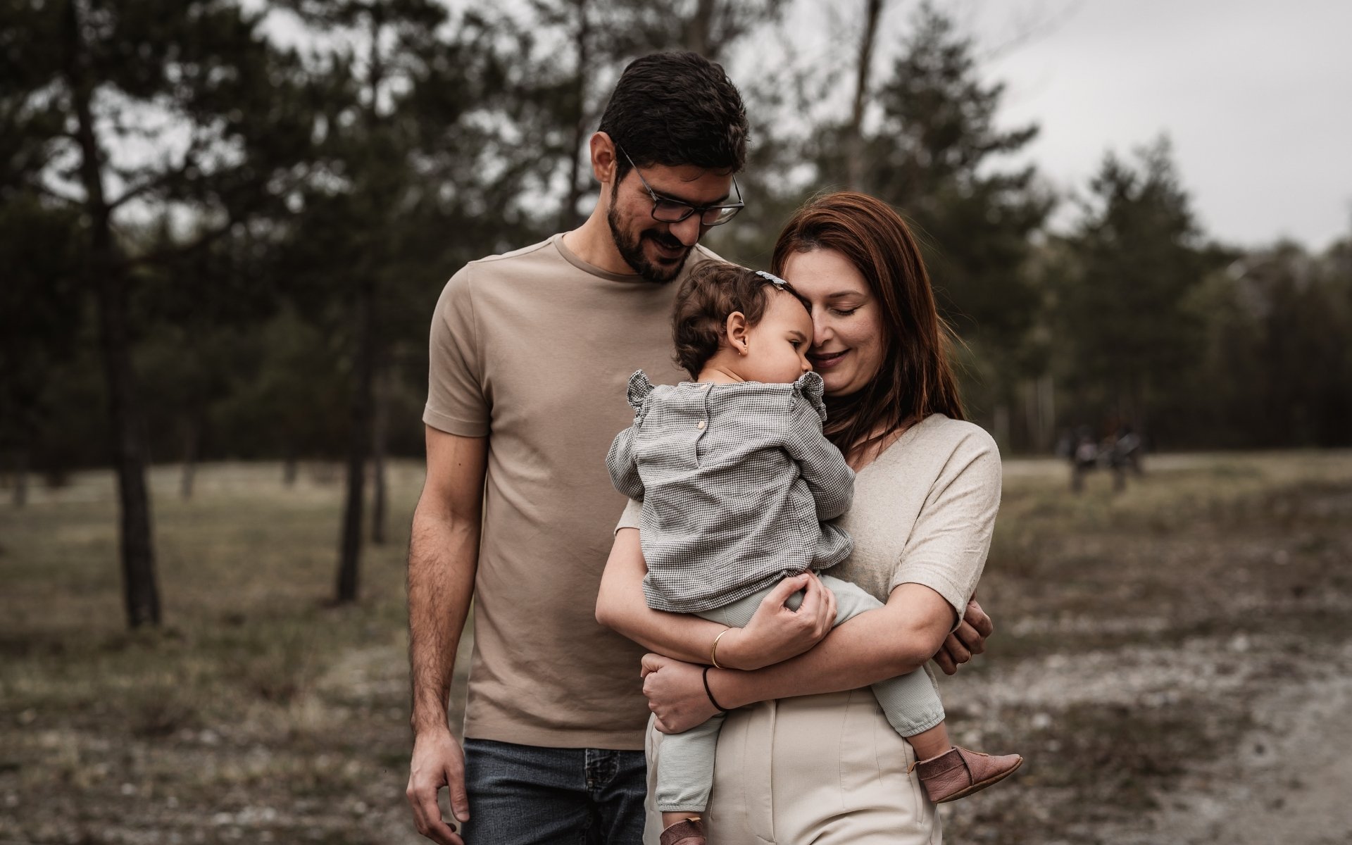 Mama, Papa und kleines Kind beim Spaziergang in der Natur. Kind ist auf den Armen der Mama und kuschelt sich an sie.