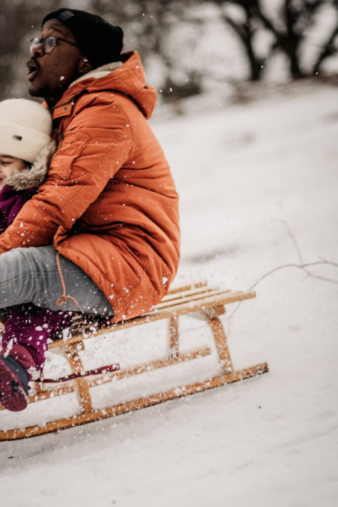 Papa mit Kleinkind im Schnee beim Schlittenfahren