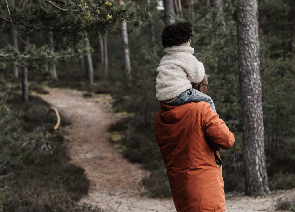 Papa mit kleinem Kind auf den Schultern im Wald