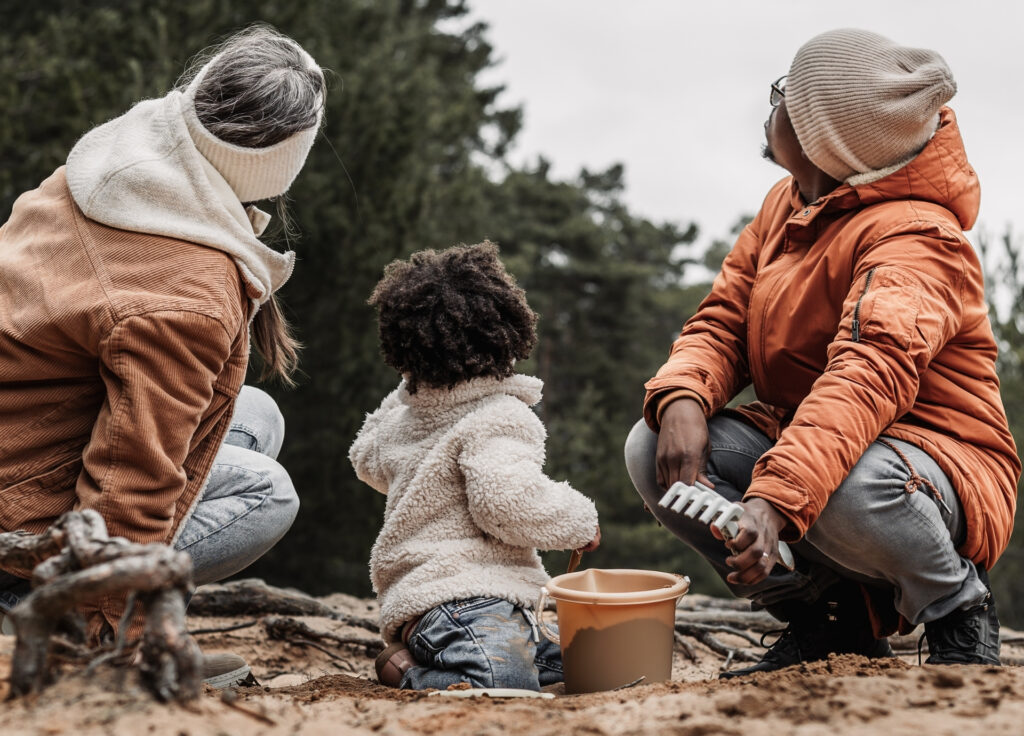 Eltern mit Tochter zwischen sich von hinten betrachtet hocken im Sand und schauen nach oben zum Horizont.