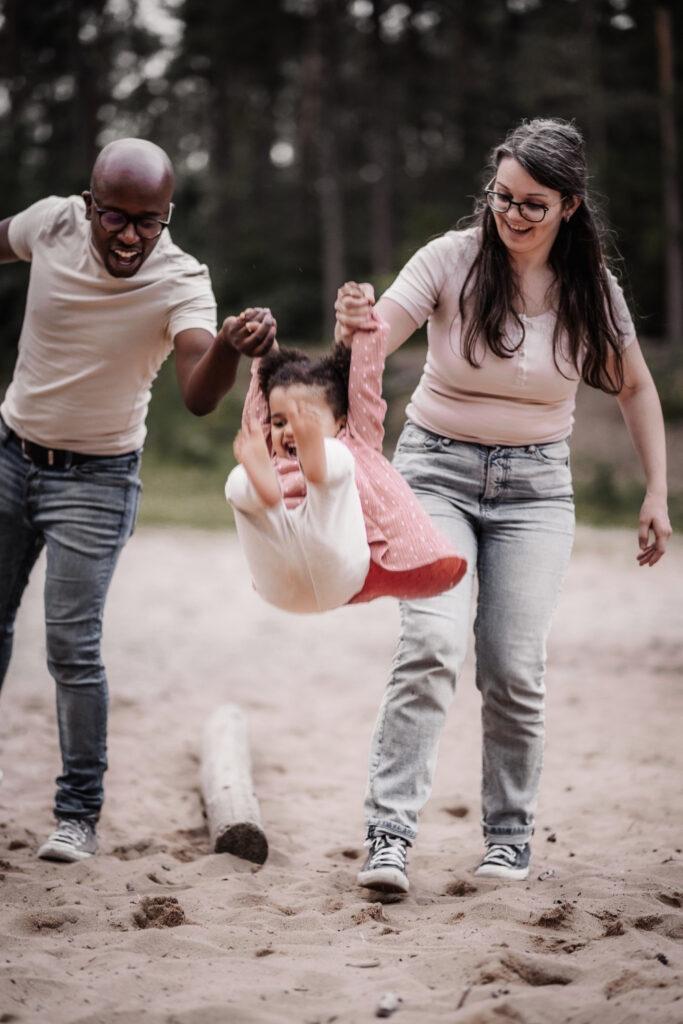 Mama, Papa und Kind auf der Sanddüne spielen Engelchen Flieg