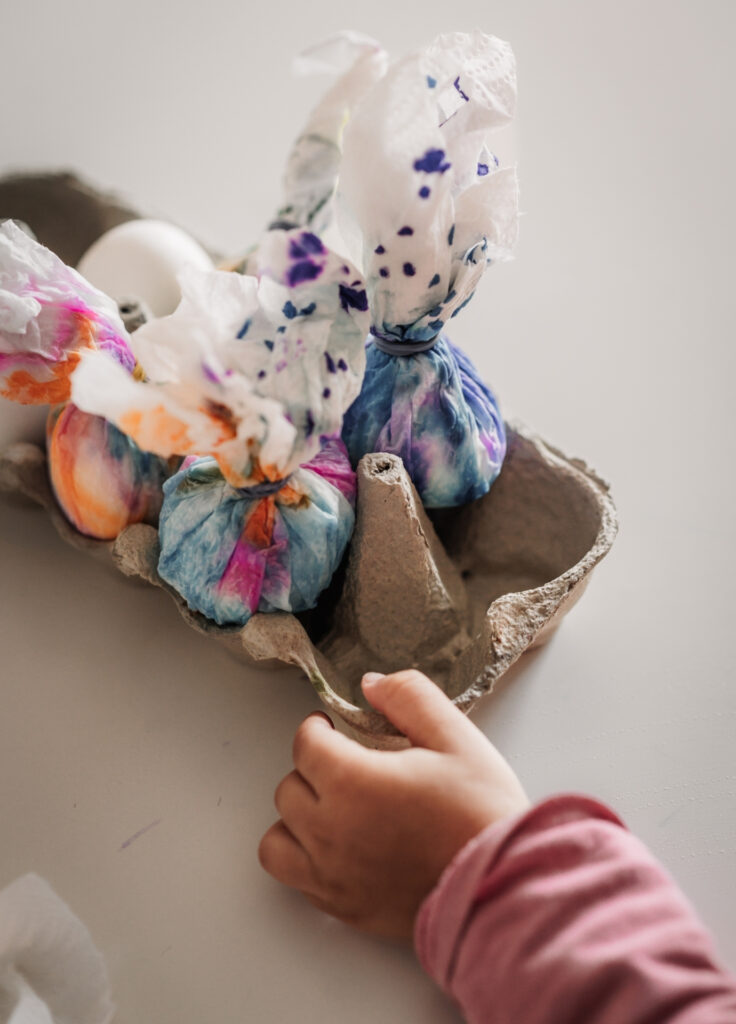 Kinderhand hält einen Eierkarton mit bunt eingewickelten Ostereiern in der Hand