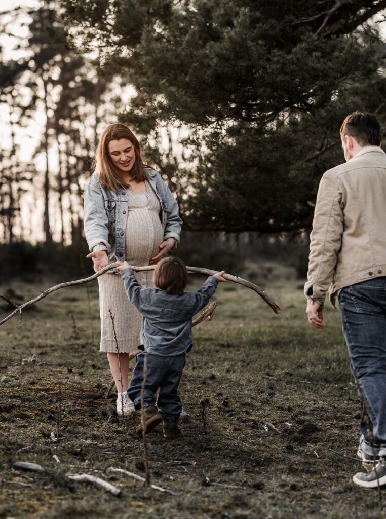 Familie mit kleinem Sohn und schwangerer Mama im Wald. Sie spielen zusammen. Der Sohn bringt Mama einen großen Ast.