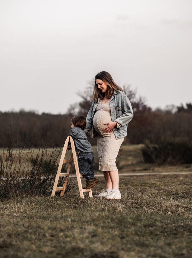 Mama mit Sohn draußen in der Natur beim Familien und Babybauchshooting. Sie genießen die gemeinsame Zeit auf einer Wiese umgeben von Wald.