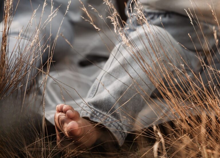 Barfüßiger Kinderfuß inmitten von Gräsern.