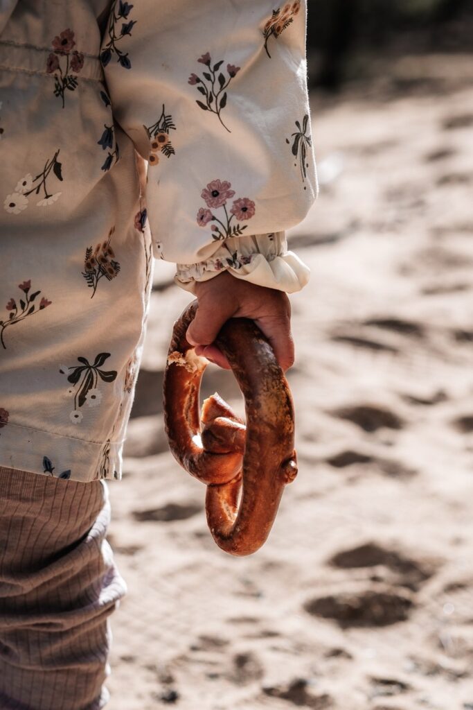 Kinderhand hält Breze - im Hintergrund ist ein sandiger Weg zu sehen.
