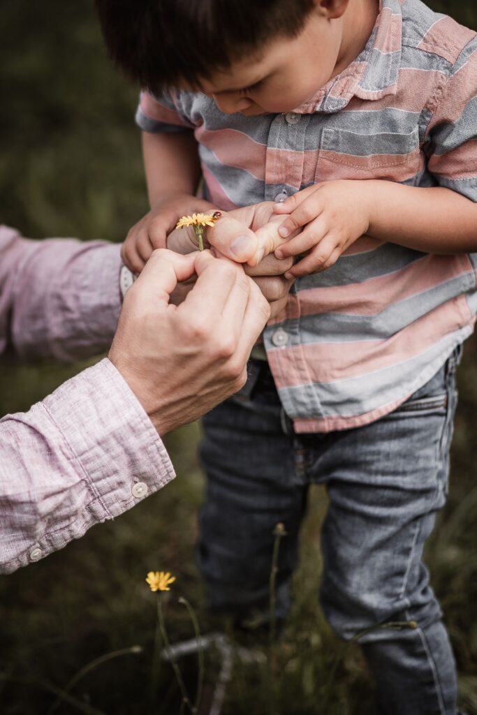 Nahaufnahme von Papa und Sohn beim Familienshooting. Sie haben ein Löwenzahl in mit Marienkäfer in der hand.