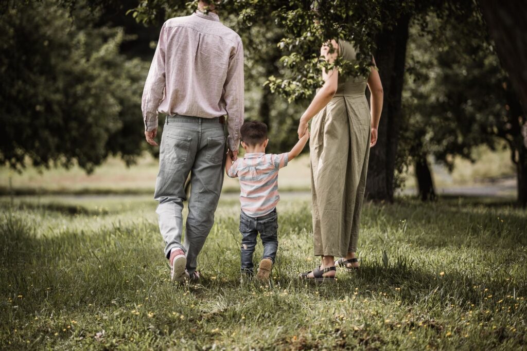 Papa, Mama und Sohn halten sich an den Händen und laufen über eine Wiese inmitten von Apfelbäumen.