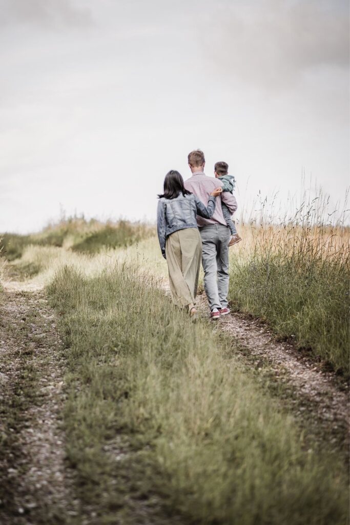 Familienfoto mit KLeinkind. Mama, Papa und Sohn laufen auf einem Feldweg weg von der Kamera.