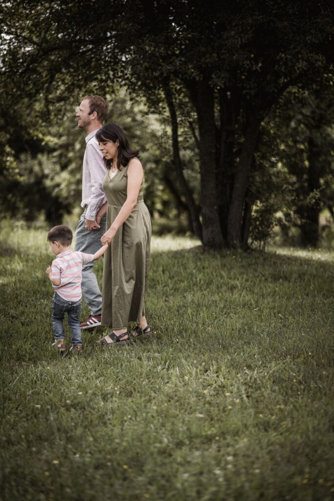 Papa, Mama und Sohn halten sich an den Händen und laufen über eine Wiese inmitten von Apfelbäumen.