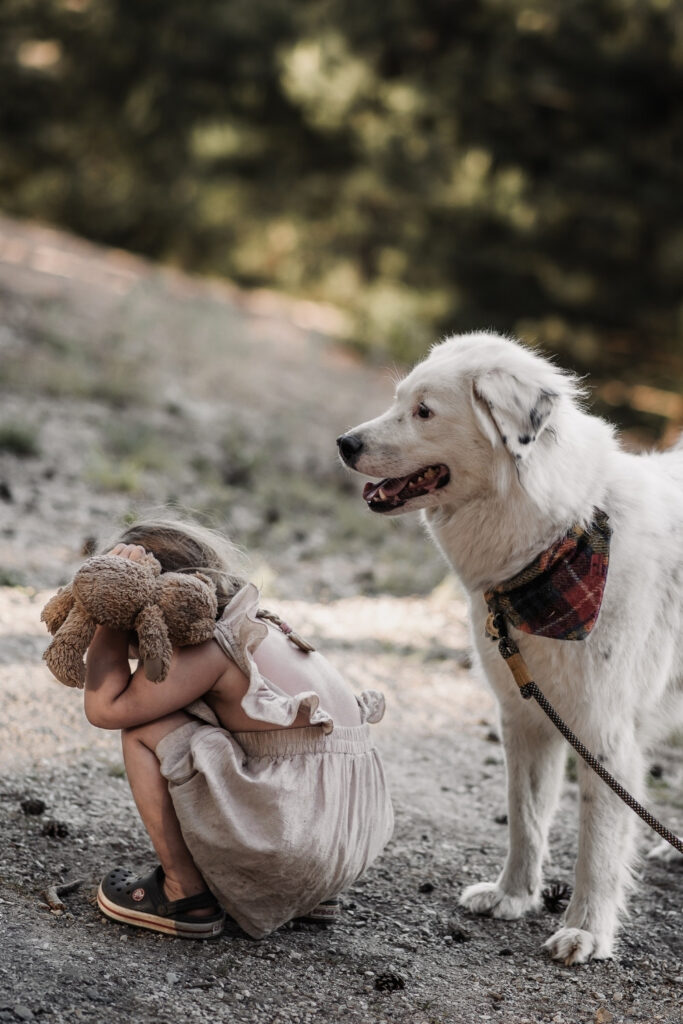 3-jähriges Mädchen hockt im Sand neben einem weißen Hund beim Familienshooting am fränkischen Dünenweg.